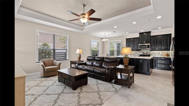 living room with light tile patterned floors, ceiling fan with notable chandelier, a textured ceiling, and a tray ceiling