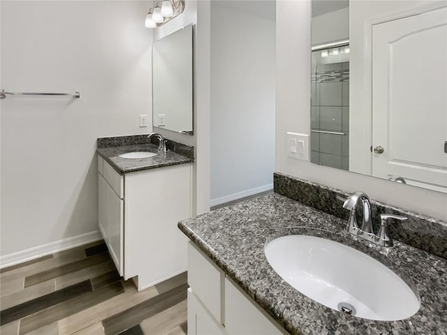 bathroom featuring wood finished floors, two vanities, baseboards, and a sink