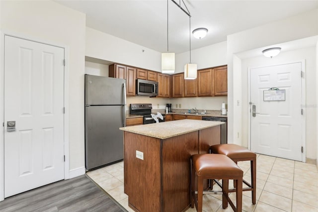 kitchen with light tile patterned flooring, appliances with stainless steel finishes, decorative light fixtures, brown cabinets, and a center island