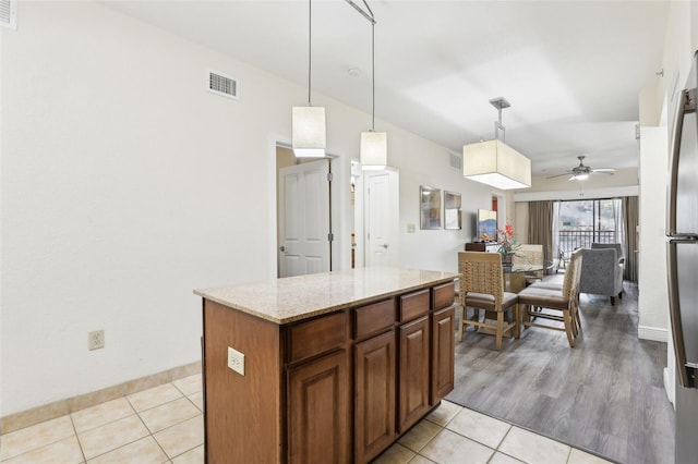 kitchen featuring visible vents, light stone counters, a kitchen island, light tile patterned floors, and hanging light fixtures