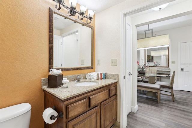 bathroom featuring vanity, wood finished floors, an inviting chandelier, toilet, and a textured wall