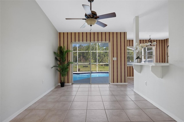 unfurnished room featuring baseboards, light tile patterned flooring, and ceiling fan with notable chandelier