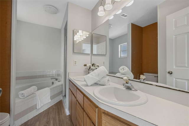 full bath featuring vanity, wood finished floors, visible vents, toilet, and a bath