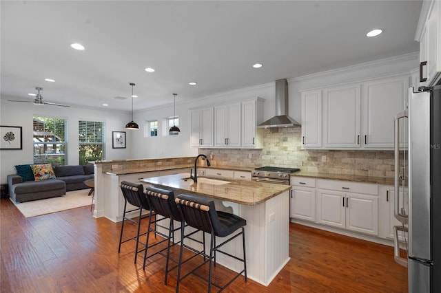 kitchen featuring wall chimney range hood, dark wood finished floors, open floor plan, stainless steel appliances, and white cabinetry