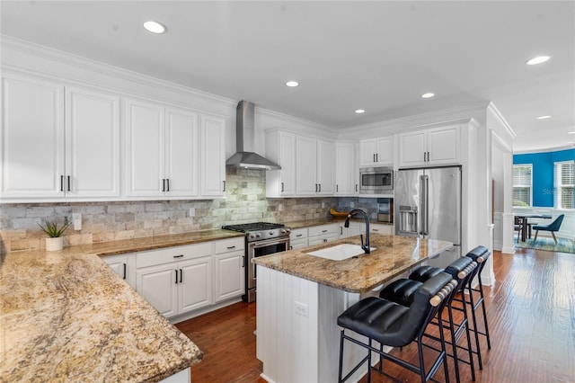 kitchen with wall chimney range hood, white cabinets, appliances with stainless steel finishes, and a sink