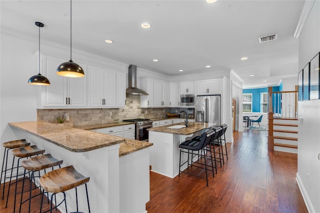 kitchen with visible vents, wall chimney range hood, a breakfast bar area, ornamental molding, and appliances with stainless steel finishes