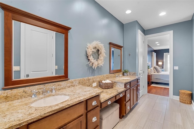 ensuite bathroom with double vanity, connected bathroom, baseboards, and a sink