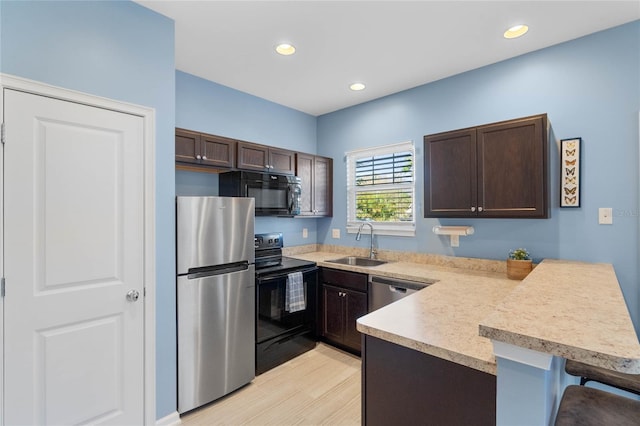 kitchen with black appliances, dark brown cabinets, a peninsula, and a sink