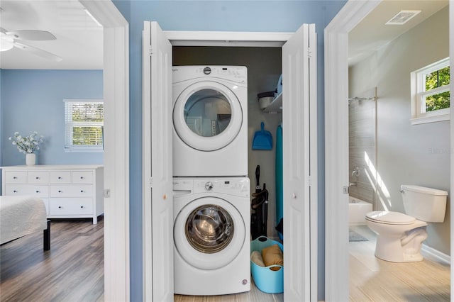 laundry room featuring visible vents, a ceiling fan, wood finished floors, stacked washer / dryer, and laundry area