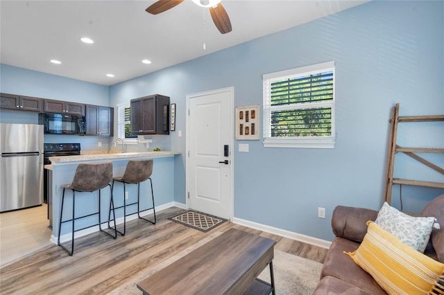 kitchen featuring dark brown cabinets, black microwave, a breakfast bar, light countertops, and freestanding refrigerator