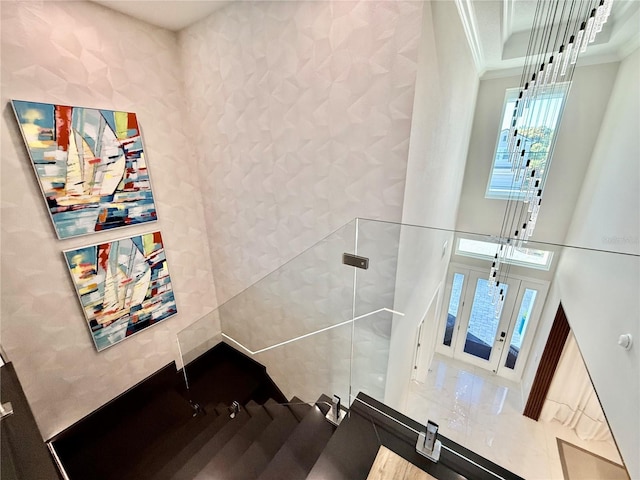 staircase featuring a raised ceiling, a high ceiling, and crown molding