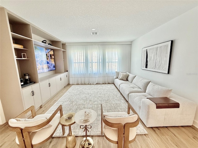 living area with visible vents, light wood-style flooring, and a textured ceiling