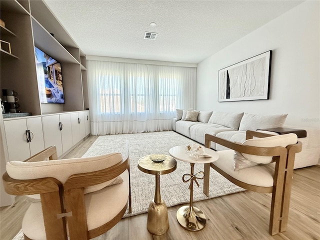 living room with visible vents, light wood finished floors, and a textured ceiling