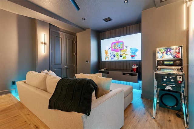 cinema room with baseboards, visible vents, light wood-type flooring, and a textured ceiling