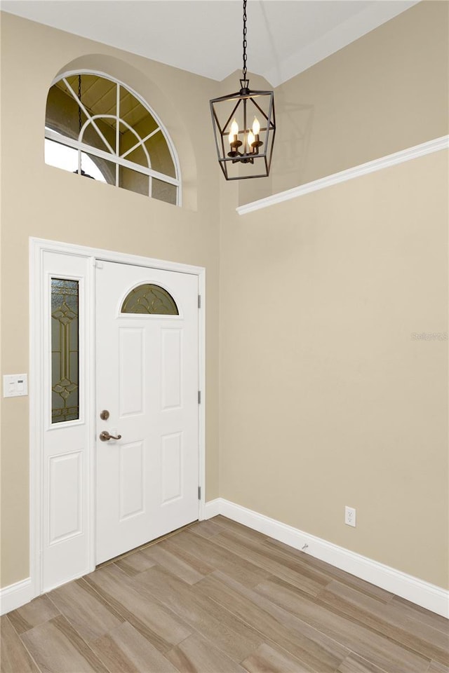 foyer entrance featuring baseboards, light wood-style floors, a high ceiling, and a chandelier