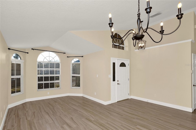 empty room featuring visible vents, baseboards, vaulted ceiling, wood finished floors, and a textured ceiling