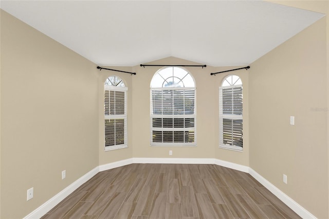 spare room featuring baseboards, lofted ceiling, and wood finished floors