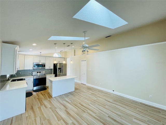 kitchen featuring a center island, lofted ceiling with skylight, decorative backsplash, appliances with stainless steel finishes, and a sink