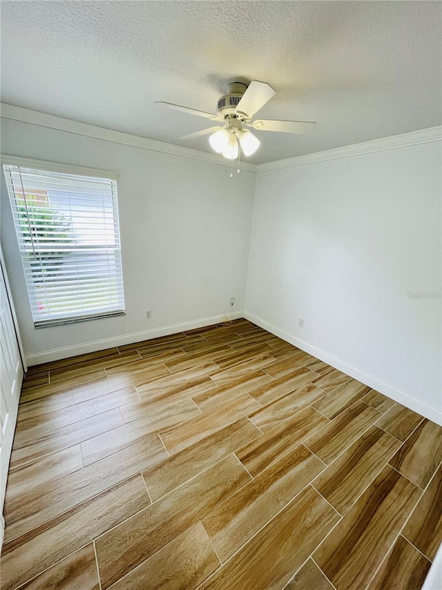 spare room featuring a ceiling fan, a textured ceiling, wood finished floors, crown molding, and baseboards