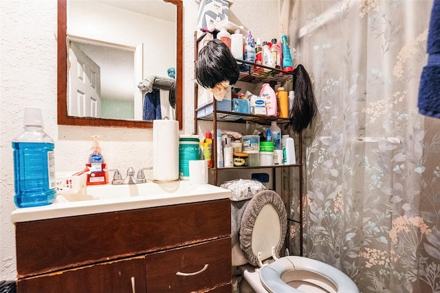 bathroom with toilet, vanity, and a textured wall