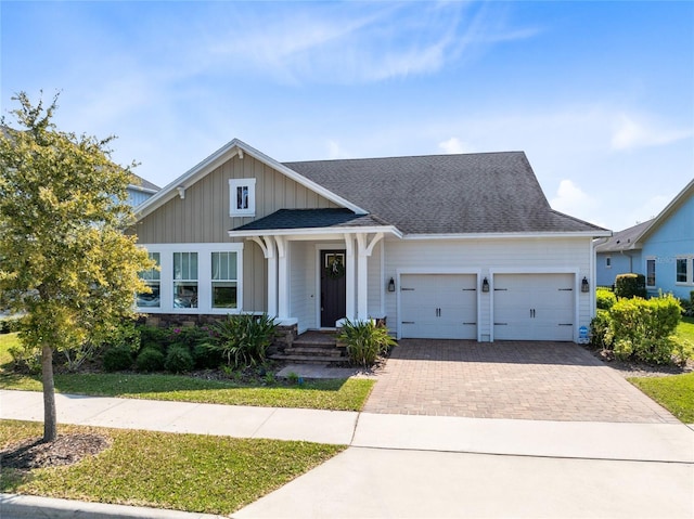 view of front facade featuring decorative driveway, board and batten siding, an attached garage, and roof with shingles