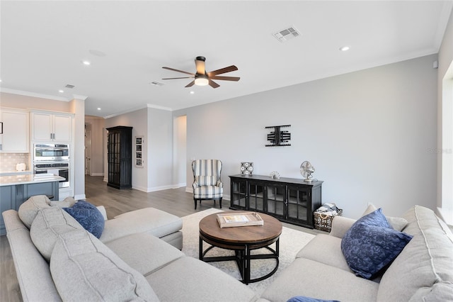 living room with light wood finished floors, visible vents, baseboards, ornamental molding, and recessed lighting