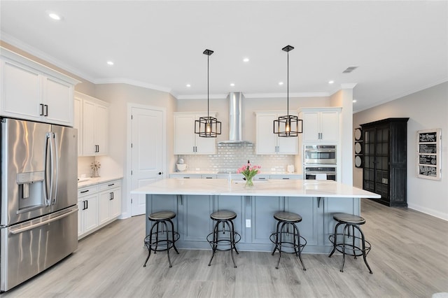 kitchen featuring light countertops, a large island with sink, stainless steel appliances, white cabinetry, and wall chimney exhaust hood