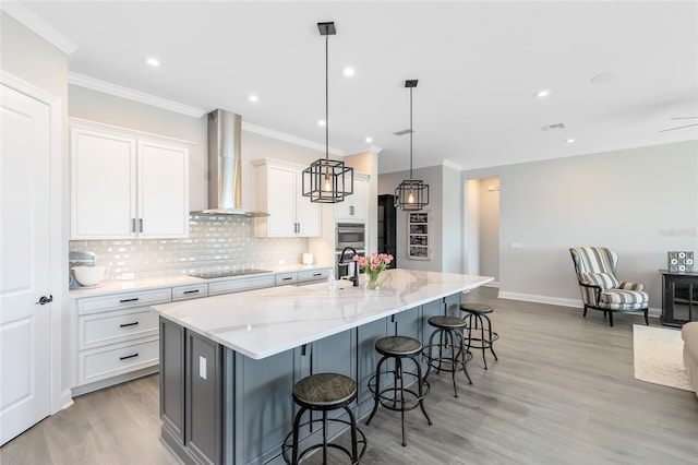 kitchen with white cabinetry, crown molding, wall chimney range hood, decorative backsplash, and a large island with sink