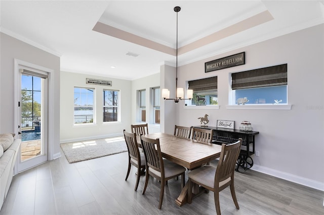 dining space with a tray ceiling, wood finished floors, visible vents, and ornamental molding