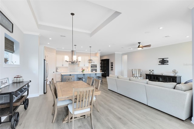 dining room featuring ornamental molding, ceiling fan with notable chandelier, recessed lighting, light wood finished floors, and a raised ceiling