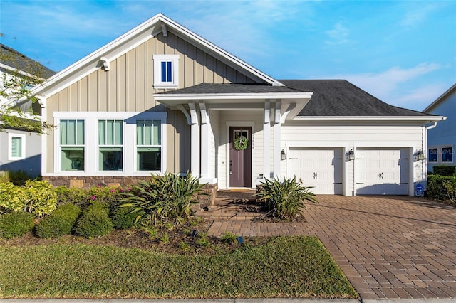 modern farmhouse featuring a shingled roof, a garage, stone siding, decorative driveway, and board and batten siding