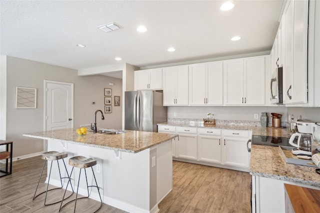 kitchen featuring a sink, appliances with stainless steel finishes, light wood-style floors, white cabinets, and a kitchen island with sink