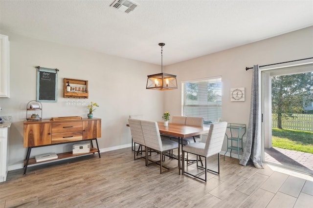 dining space featuring visible vents, light wood-style flooring, a textured ceiling, an inviting chandelier, and baseboards