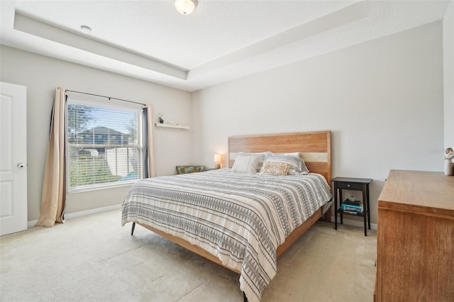 bedroom featuring light carpet, a tray ceiling, and baseboards