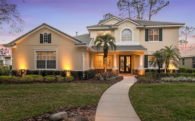 view of front of house featuring a tiled roof, stucco siding, french doors, and a front lawn