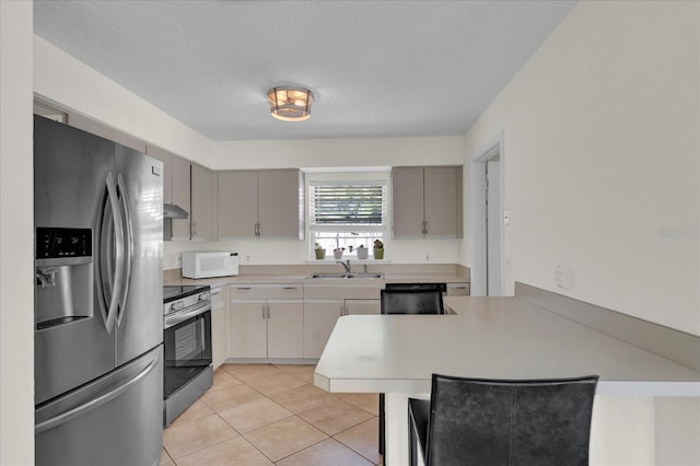 kitchen with a sink, appliances with stainless steel finishes, a peninsula, light countertops, and light tile patterned floors