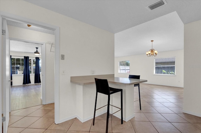 kitchen featuring a breakfast bar area, light tile patterned floors, visible vents, hanging light fixtures, and a chandelier