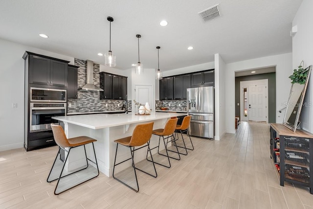 kitchen featuring visible vents, wall chimney range hood, stainless steel appliances, light wood finished floors, and light countertops