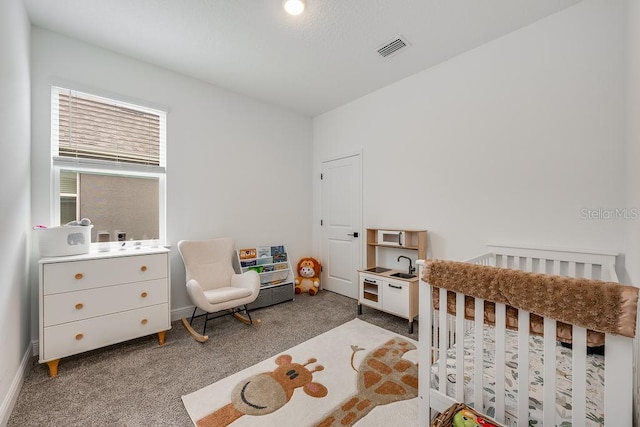 bedroom with visible vents, a crib, carpet, and baseboards