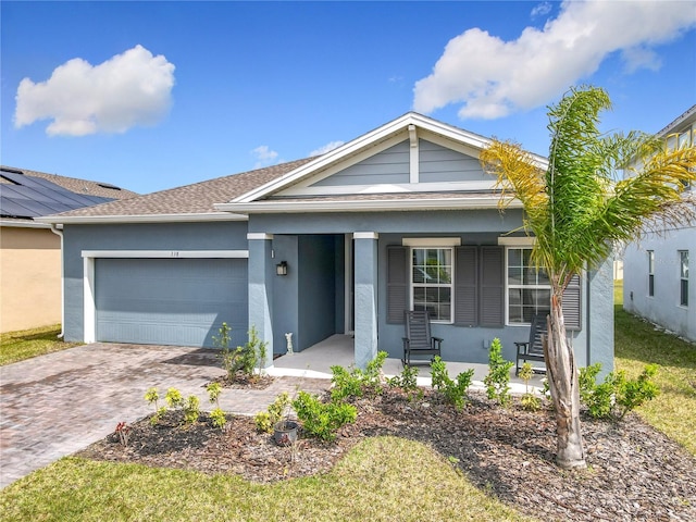 single story home with a porch, decorative driveway, a garage, and stucco siding