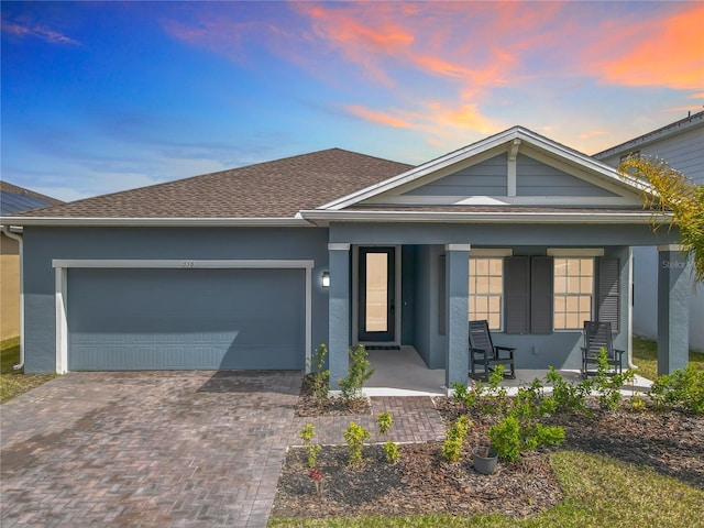 view of front of property with roof with shingles, a porch, an attached garage, stucco siding, and decorative driveway