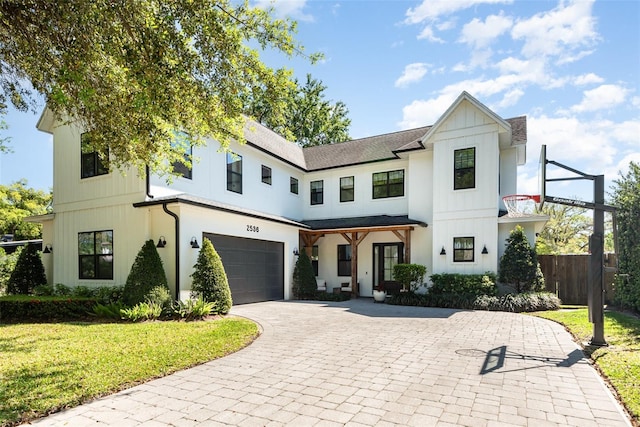 modern farmhouse with a front yard, fence, a garage, decorative driveway, and board and batten siding