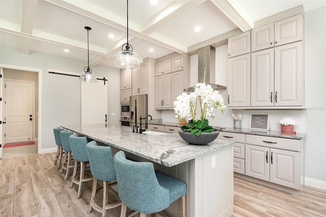 kitchen with beamed ceiling, light wood-style floors, wall chimney range hood, and a sink