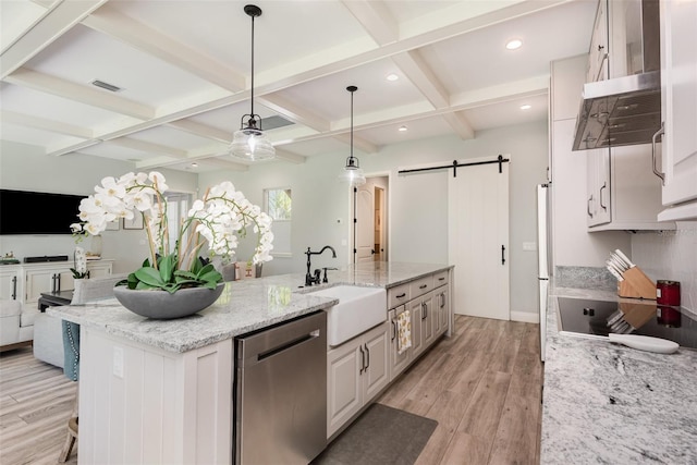 kitchen with a sink, light wood-type flooring, a barn door, stainless steel appliances, and a kitchen island with sink