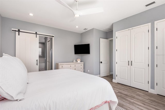 bedroom featuring visible vents, two closets, a barn door, recessed lighting, and wood finished floors