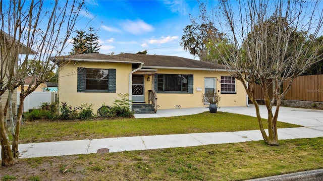 ranch-style home with entry steps, a front yard, fence, and a shingled roof