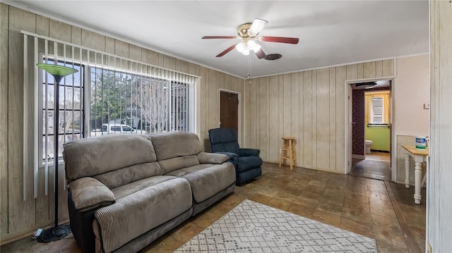 living area with wooden walls, ceiling fan, and crown molding