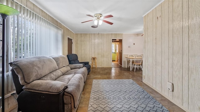 living area with wooden walls, a ceiling fan, and ornamental molding