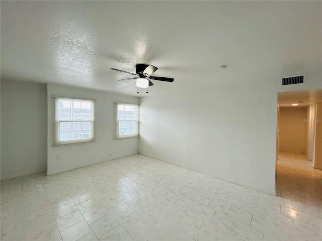 empty room featuring visible vents, a textured ceiling, marble finish floor, and a ceiling fan