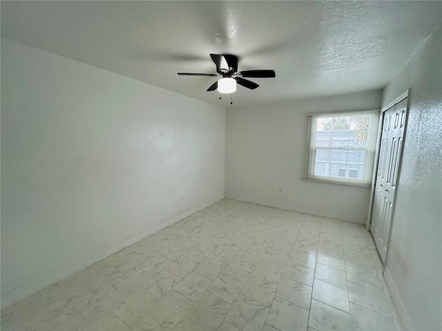 spare room with ceiling fan, baseboards, marble finish floor, and a textured ceiling